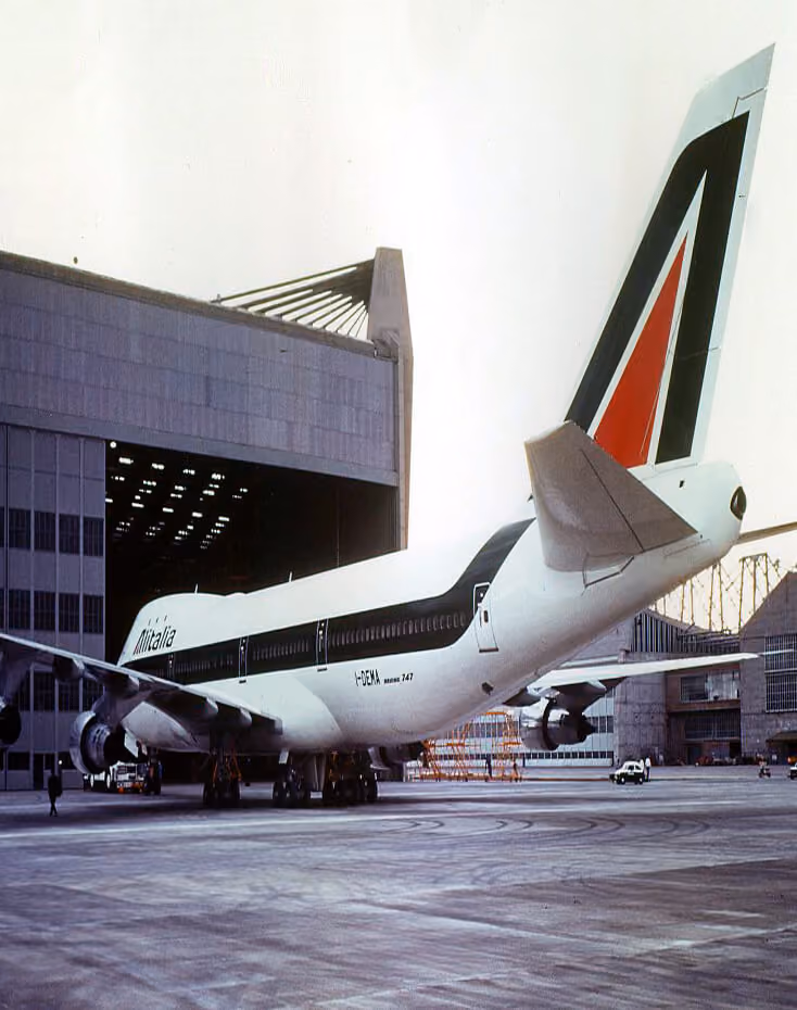Alitalia Boeing 747 airplane parked outside a large hangar at an airport.